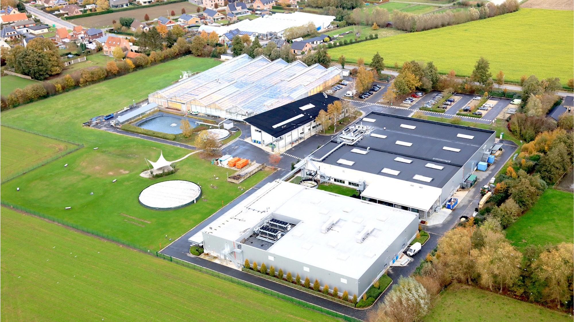 Luftaufnahme eines landwirtschaftlichen Forschungszentrums mit Gewächshäusern, Gebäuden und umliegenden Feldern.