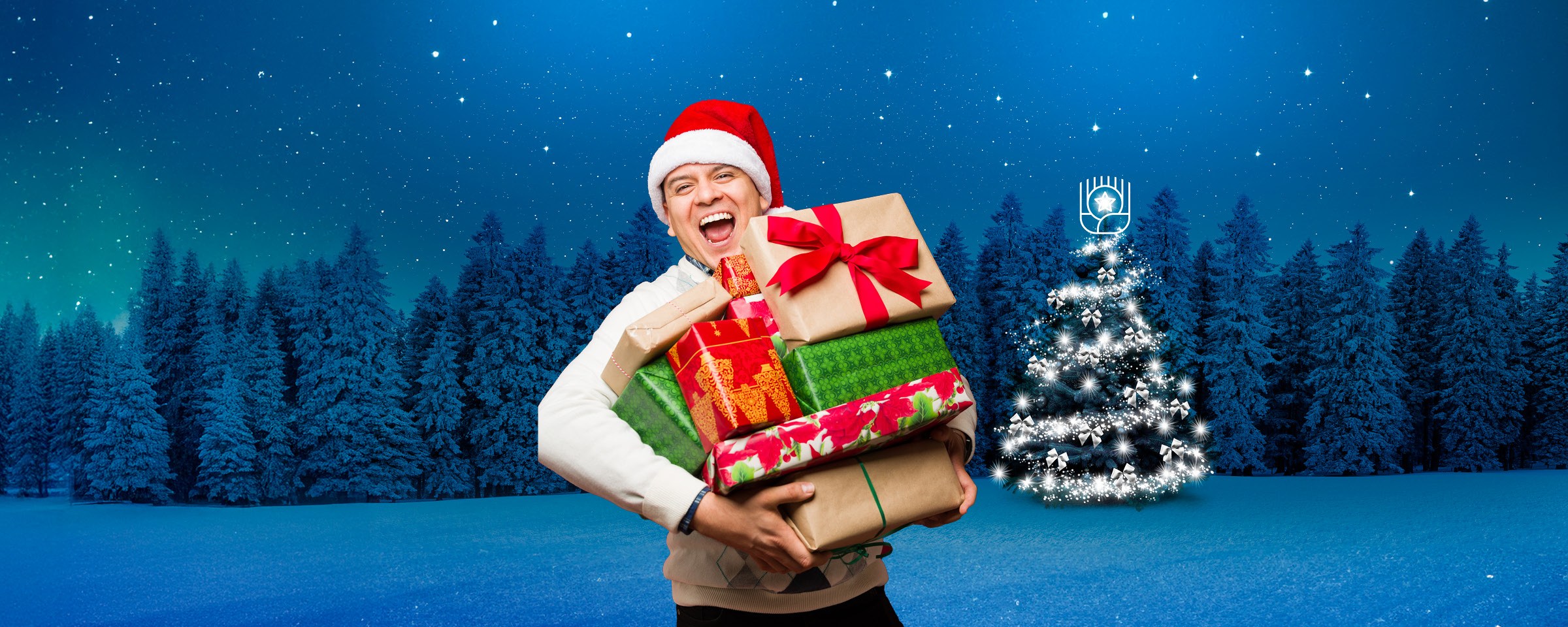 Lachender Mann mit Weihnachtsmütze trägt viele Geschenke vor verschneitem Wald und leuchtendem Weihnachtsbaum.
